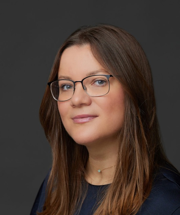Dr. Svetlana Olteanu, wearing thin dark-rimmed glasses, in front of a dark grey background